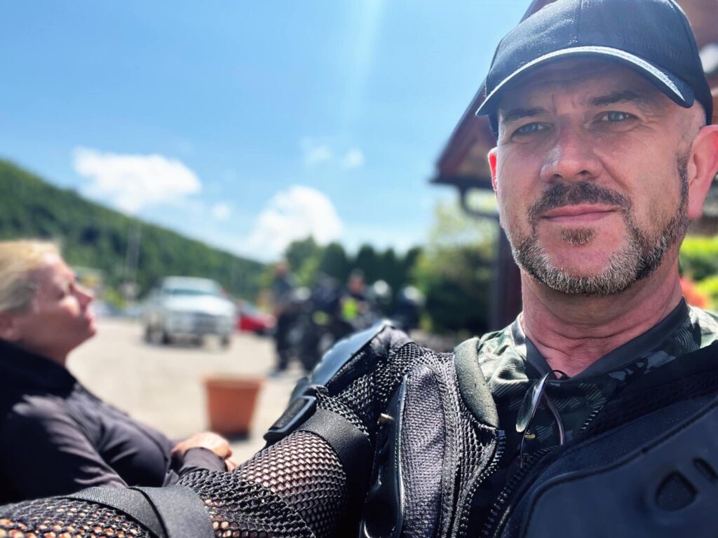 Rag with beard and baseball hat on a selfie with the Bosnian landscape behind him.