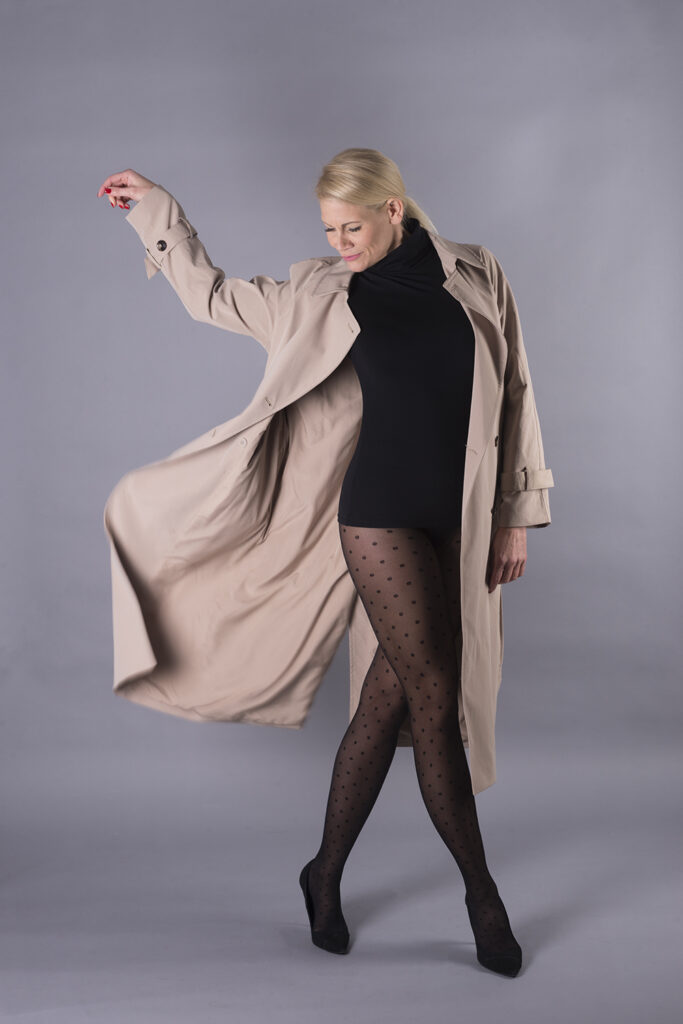 SophieS lifestyle shoot in black heels and dotted pantyhose with a long raincoat over the top.