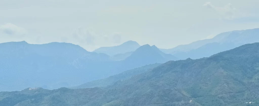 Cloudy mountain range view with a blue tint and light blue sky.