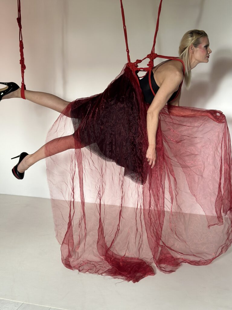 SophieS wearing black while hung from the roof of the studio with ref ropes and red organza wrapped around her.