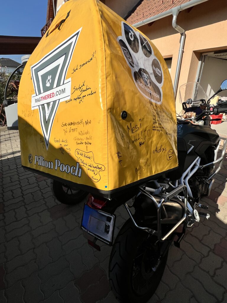 Backside view of a motorcycle focusing on a dog box which now has the ragthered.com stickers and lots of signature on it.