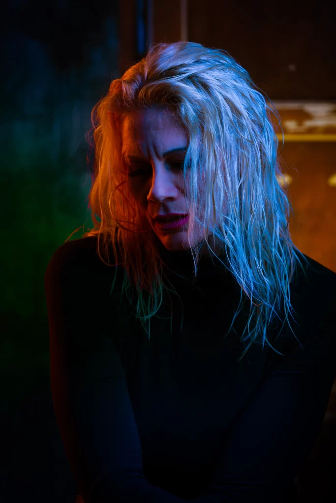 Dark image of SophieS where red and blue lighting bounces on her blond hair.