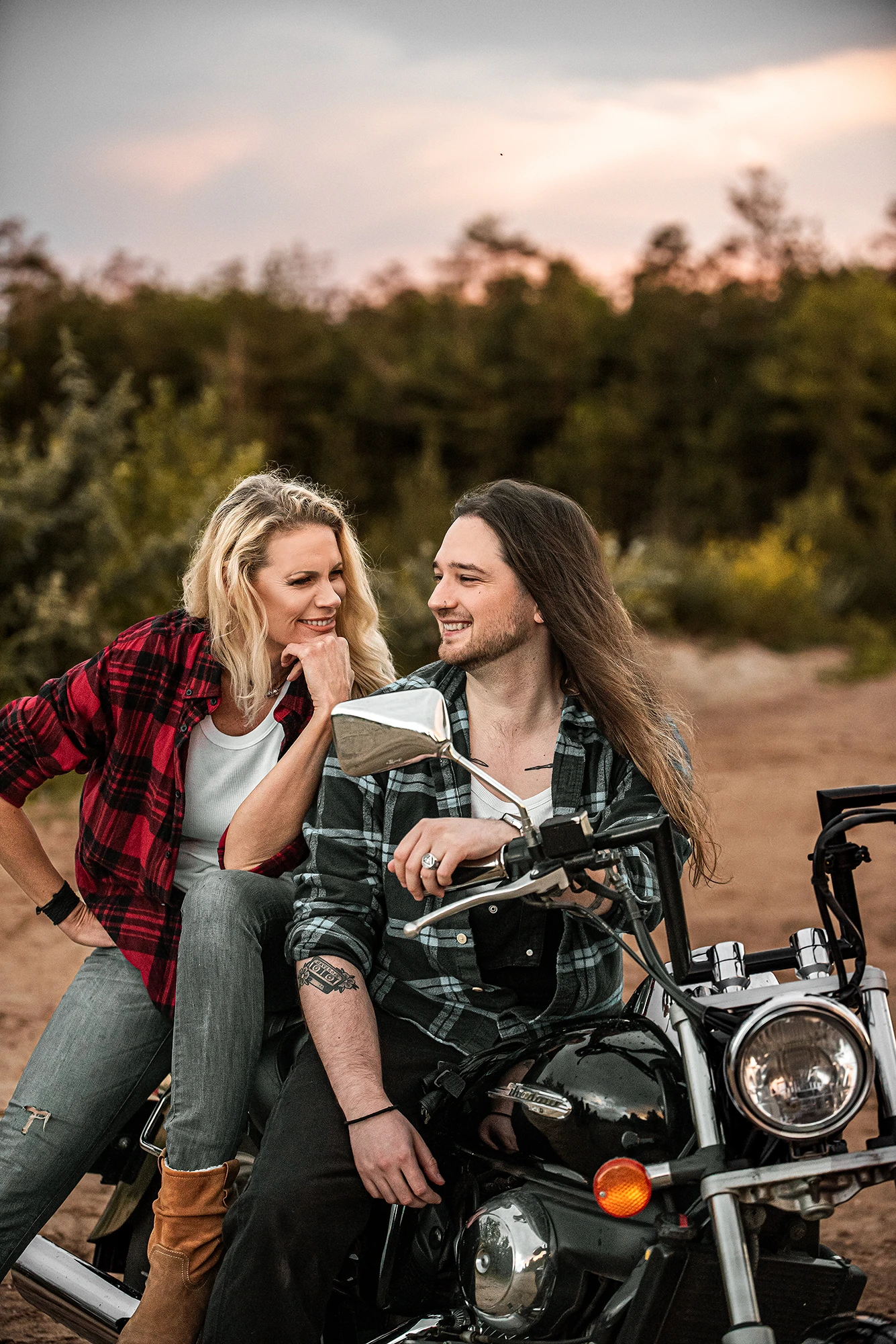 SophieS posing with a young male partner on a classic bike, looking and smiling at each other.