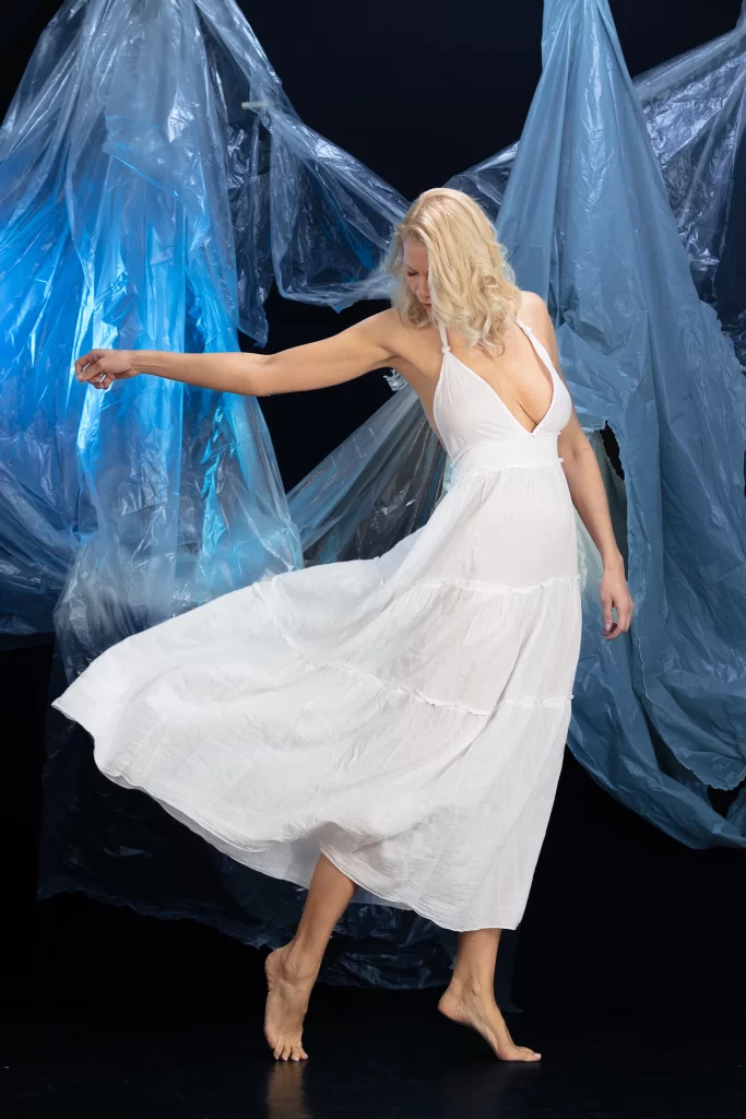 SophieS wearing a white dress which flows as she spins around in front of a dark background.