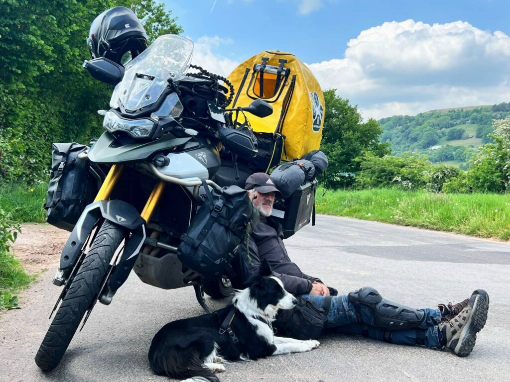 Ken és Molly ülnek a motor árnyékában, mint két megfáradt utazó a gyönyörű zöld dombos háttér előtt.