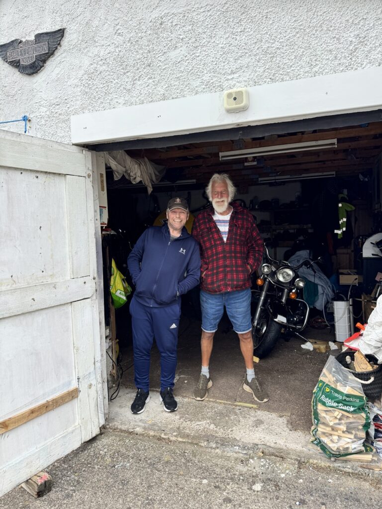 Sammy és Alex pózol a garázs előtt, mögöttük az egyik Harley lámpája kandikál.